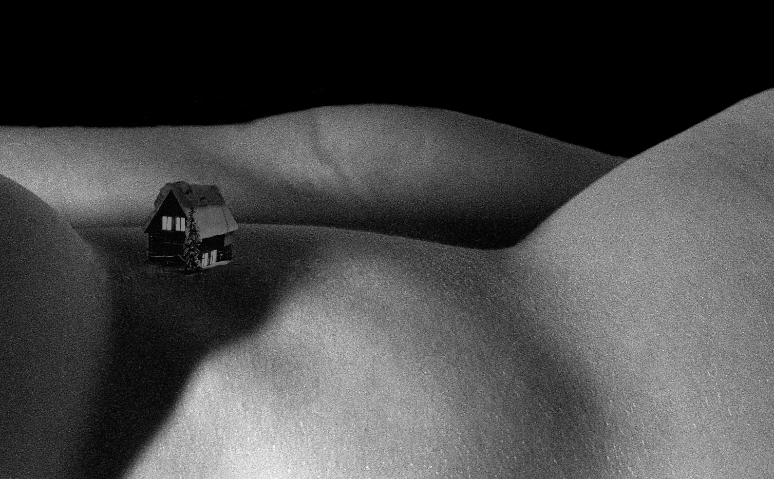 A small wooden cabin resting in a valley between two snowed hills that are really a body